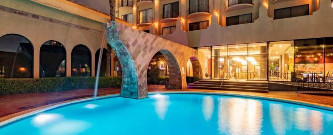 Hotel Lucerna Ciudad Juarez – alberca nocturna iluminada con arco tipo acueducto y fachada con balcones.