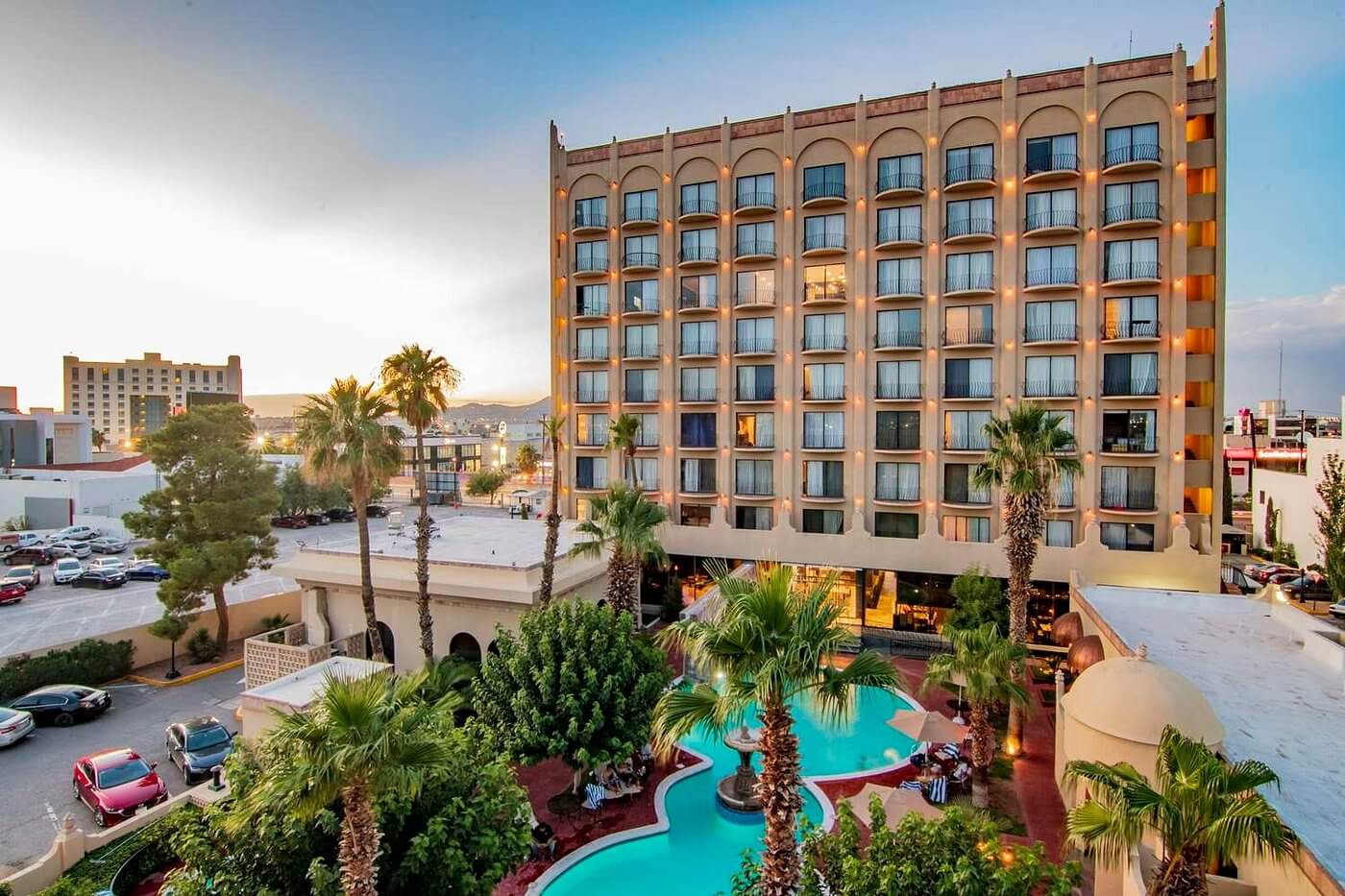Hotel Lucerna Ciudad Juarez – fachada diurna con alberca rodeada de palmeras y área central de Zona Pronaf.