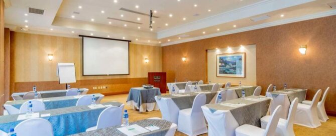 Hotel Lucerna Ciudad Juarez – salón de eventos montado en escuela con proyector, mesas y sillas blancas.