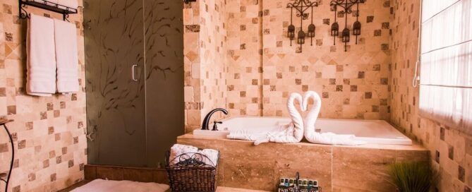 Baño con jacuzzi de mármol, toallas en forma de cisnes y regadera de vidrio esmerilado; amenidades colocadas en charola.