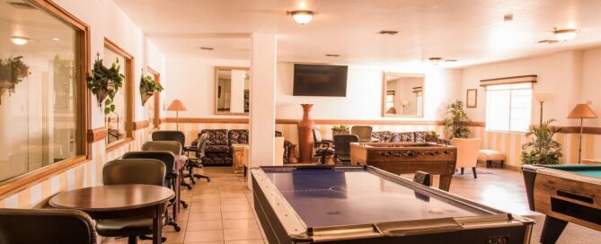 Sala de juegos con mesa de air hockey, futbolito y mesas de billar; área de descanso y TV al fondo en María Bonita Business Hotel & Suites.