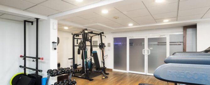 Gimnasio del Hotel Mesaluna con caminadoras Precor, mancuernas y equipo multifuncional en piso de madera.