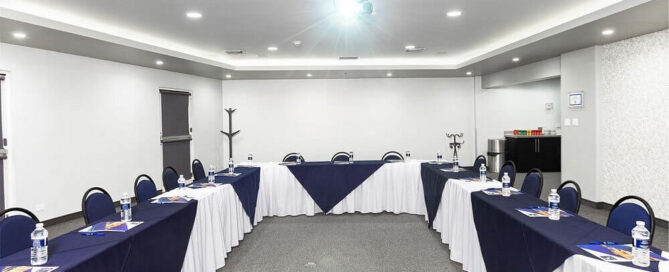 Sala de conferencias del Hotel Mesaluna en montaje tipo U con mantelería azul, proyector y estación de coffee break.