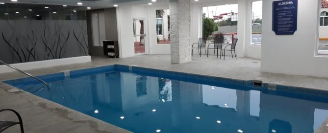Alberca interior climatizada de Krystal Urban Ciudad Juárez con barandal de acceso y ventanales perimetrales.