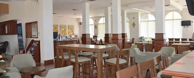 Comedor–cafetería de Krystal Urban Ciudad Juárez con mesas altas y sillas de madera en salón claro.
