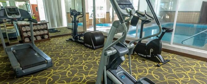 Gimnasio de Krystal Urban Ciudad Juárez con elíptica, caminadora y vista a la alberca techada tras muro de vidrio.