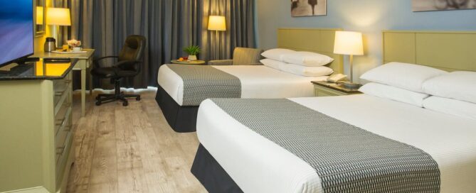 Habitación doble en Krystal Urban Ciudad Juárez con dos camas matrimoniales, escritorio con silla ergonómica y luz cálida.