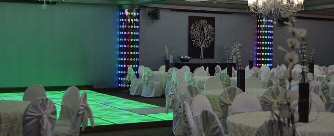 Salón de eventos del María Bonita Branch Hotel Business & Suites con iluminación morada y mesas vestidas de blanco.