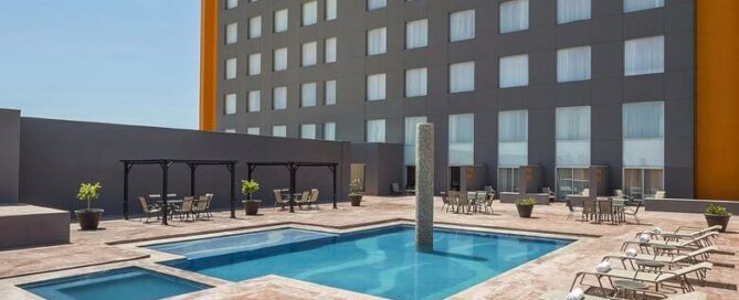 Alberca exterior del Real Inn Ciudad Juárez con chapoteadero, camastros y patio soleado.