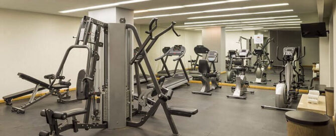 Gimnasio del Real Inn Ciudad Juárez con máquinas de pesas, caminadoras y espejo de pared completo.