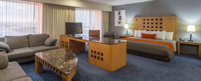 Suite amplia en Real Inn Ciudad Juárez con cama king, sala, escritorio y TV frente a ventanales.