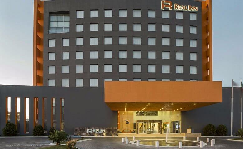 Fachada del Real Inn Ciudad Juárez con marquesina naranja y entrada principal al atardecer.