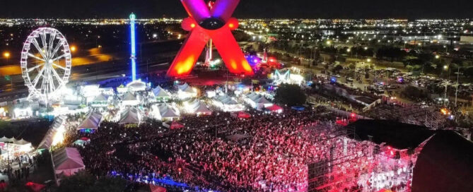 Vista aérea nocturna de la Feria Juárez en la Plaza de la Mexicanidad con La X iluminada, rueda de la fortuna y escenario; foto de El Diario de Juárez.