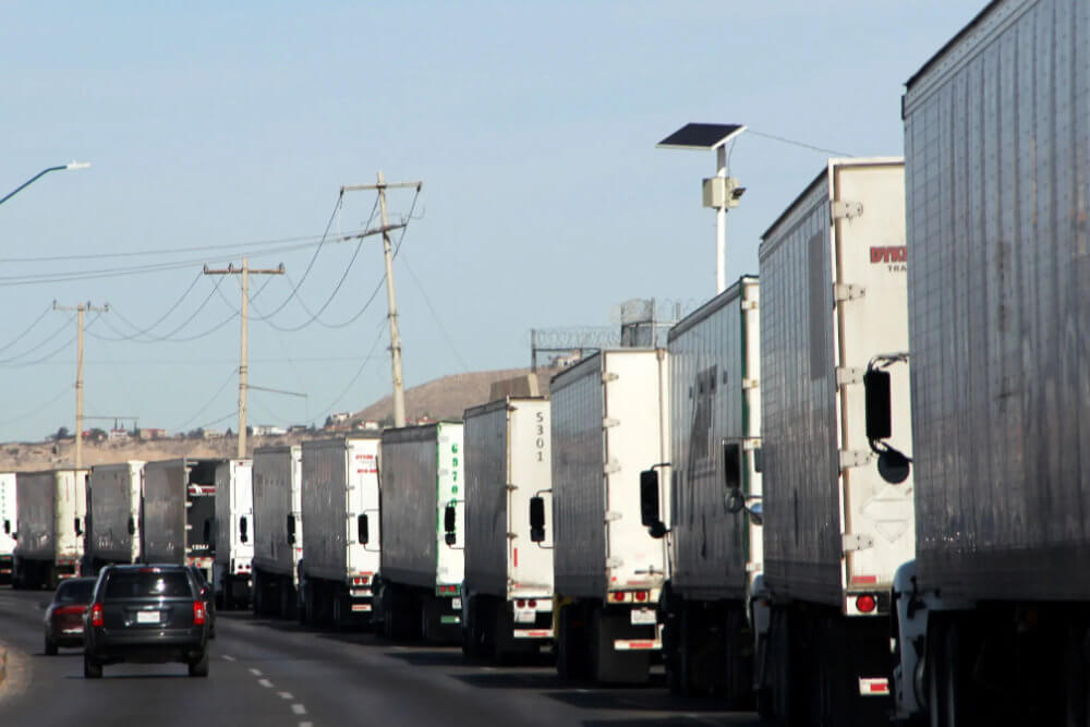 Fila de camiones de carga en cruce fronterizo en Ciudad Juarez y El Paso Fila de tráileres rumbo al cruce fronterizo Ciudad Juárez–El Paso en carril de exportación, vista lateral sobre la carretera.