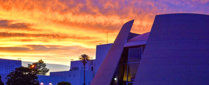 Fachada del Museo de Arte de Ciudad Juárez al atardecer, con cielo anaranjado y azul sobre el edificio modernista de la Zona Pronaf.