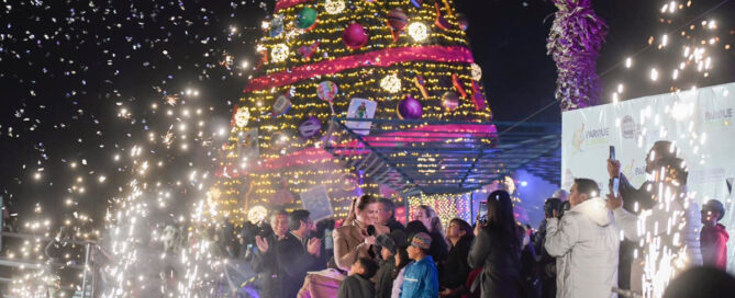 Celebración navideña en el Parque Central de Ciudad Juárez con árbol iluminado, público asistente y juegos mecánicos durante el encendido decembrino.