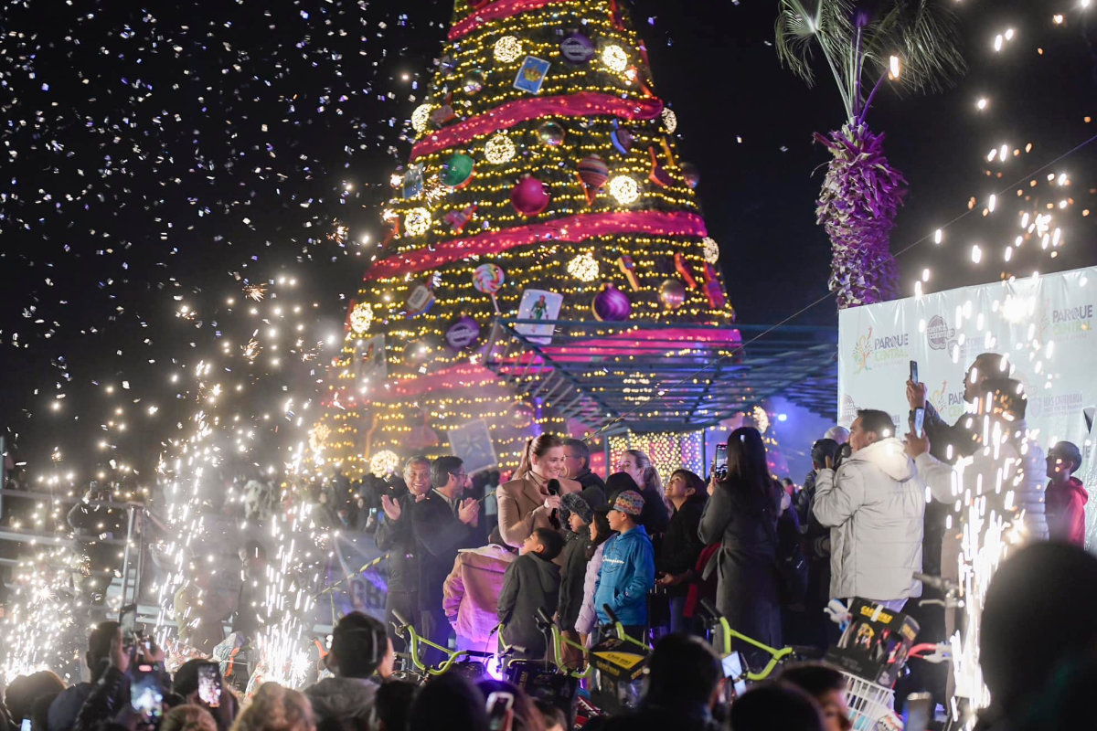 Celebración navideña en el Parque Central de Ciudad Juárez con árbol iluminado, público asistente y juegos mecánicos durante el encendido decembrino.