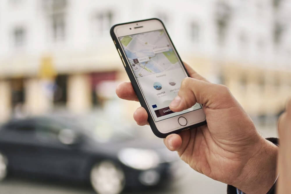 Uber en Ciudad Juarez para solicitar un viaje Manos usando la app de Uber para pedir un viaje en Ciudad Juárez, con auto desenfocado al fondo.