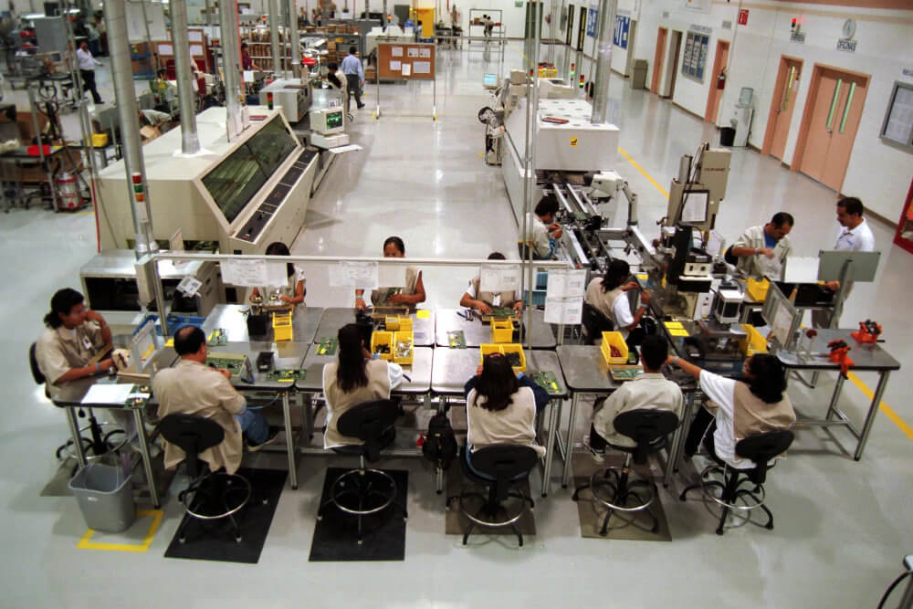 ciudad juarez maquiladora trabajadores en linea de ensamble Trabajadores en maquiladora de Ciudad Juárez en línea de ensamble, con equipo industrial y supervisión en planta.