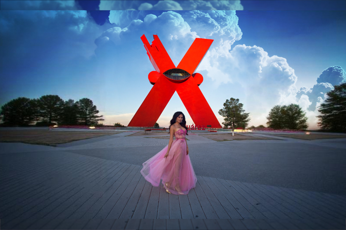 Andrea Meza vestida de rosa posando frente al Monumento a la Mexicanidad, La X, en la Plaza de la Mexicanidad de Ciudad Juárez.