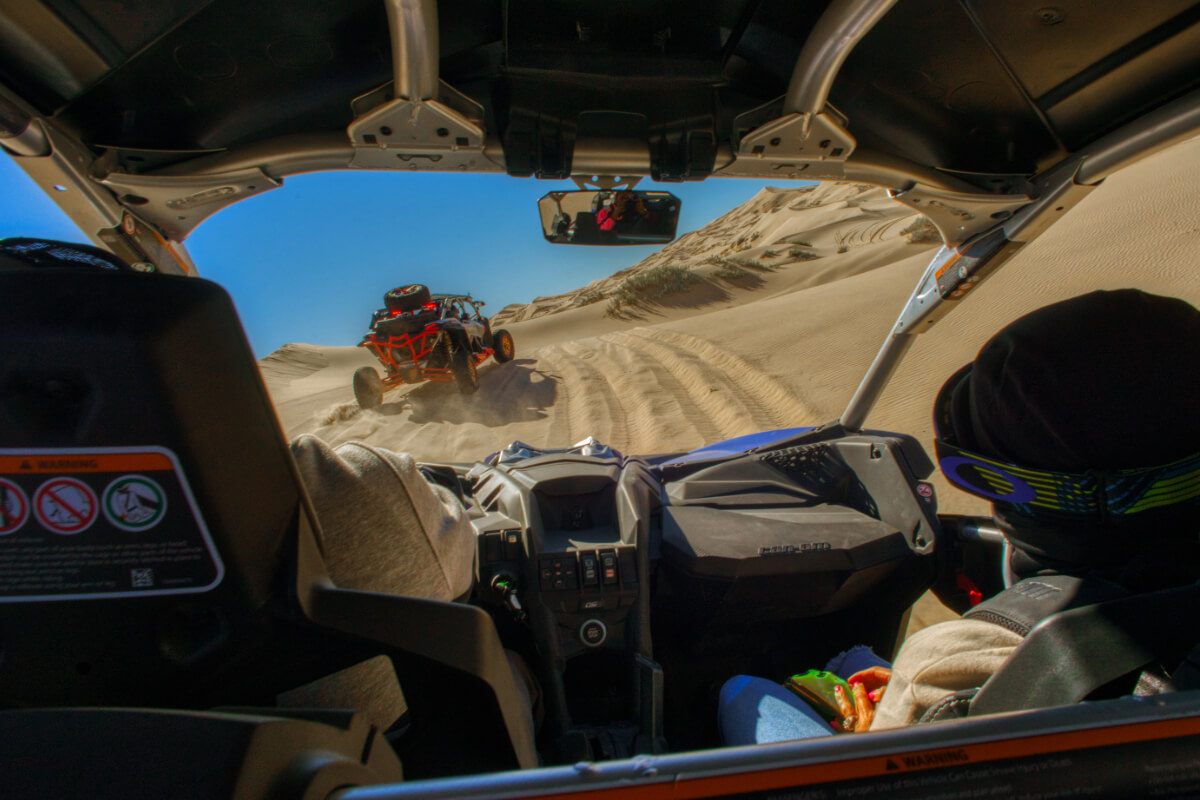 Cabina de vehículo ATV recorriendo dunas del desierto de Samalayuca, con otro vehículo adelante levantando arena y paisaje de dunas al fondo.