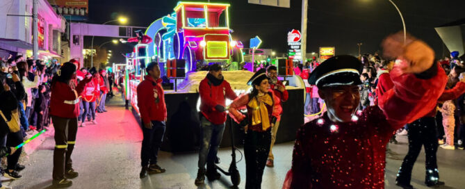 Desfile navideño de la Caravana Coca-Cola en Ciudad Juárez, con carro alegórico iluminado y bailarines saludando al público en la calle.