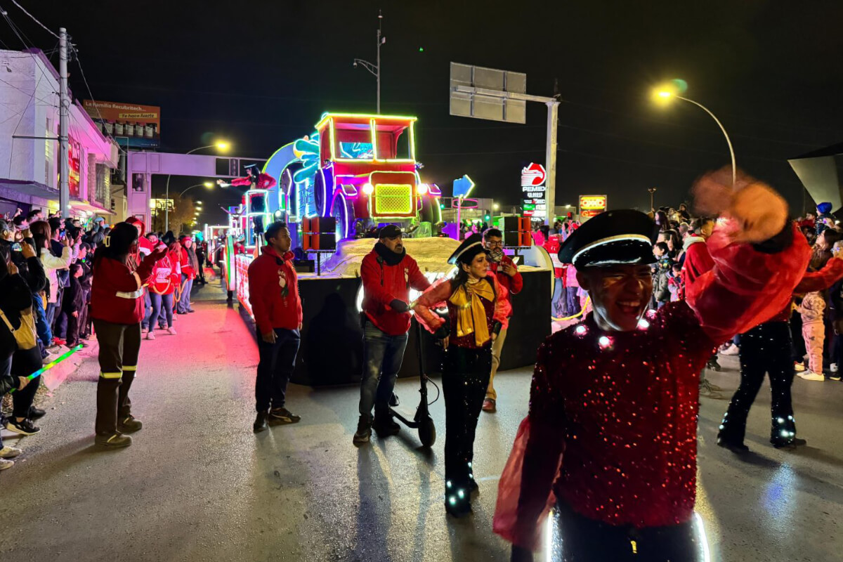 Desfile navideño de la Caravana Coca-Cola en Ciudad Juárez, con carro alegórico iluminado y bailarines saludando al público en la calle.