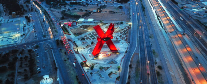 Vista aérea nocturna del Monumento a la Mexicanidad, La X, en la Plaza de la Mexicanidad de Ciudad Juárez, rodeado de avenidas iluminadas.