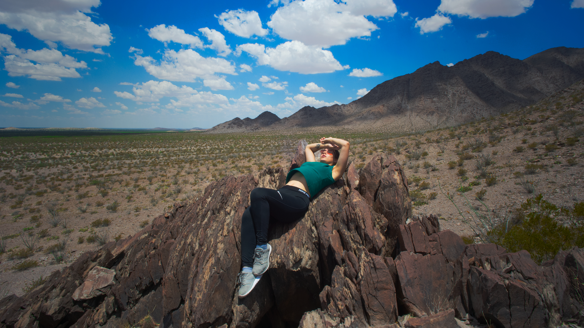 Visitante descansando sobre rocas en la sierra cercana a Ciudad Juárez, con paisaje desértico y montañas al fondo.