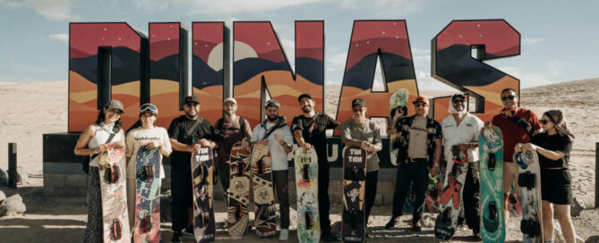 Participantes de Descubre Juárez con tablas de sandboarding frente al letrero de las Dunas de Samalayuca